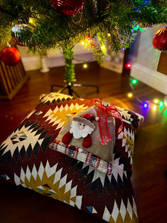 Christmas Present Under the Xmas Tree with Pillow and Santa Claus Pattern. Colorful Led Lights. Concept Photography.の写真素材