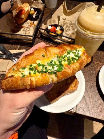 Croissant sandwich with egg holding in hand at cafe shop restaurant served in tray.