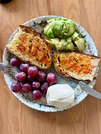 Healthy protein breakfast plate with purple grapes avocado and cream cheese on wooden tableの写真素材