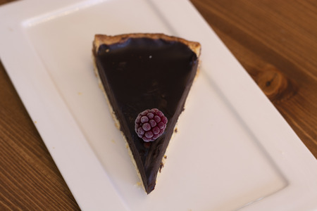 Fresh baked chocolate tart with raspberry on top served on white plate with isolated black...