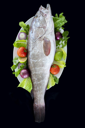 White grouper fish with rockets leaves, tomatoes, onions and lemon served on plate with black backgroundの写真素材