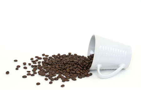 A cup of coffee beans has spilled onto a white background.の写真素材