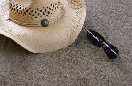A hat and sunglasses are on the sand.の写真素材