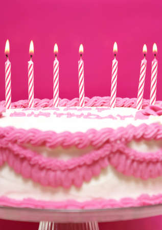 Lit birthday candles on a pink cake are waiting to be blown out as a wish is being made.の写真素材