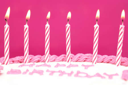 Lit birthday candles on a pink cake are waiting to be blown out as a wish is being made.の写真素材