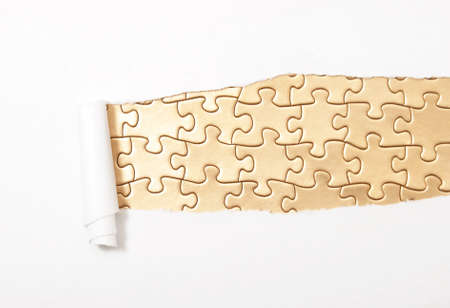 A conceptual piece where a golden puzzle is breaking through the paper.の写真素材