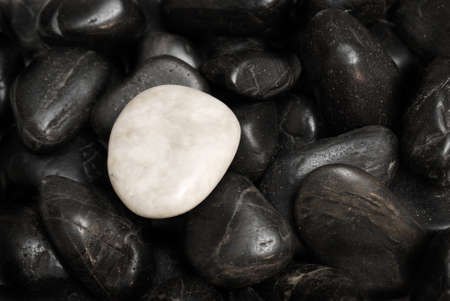 A white stone surrounded by other black stones for a conceptual difference.の写真素材