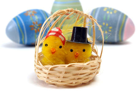 A couple of chicks in a basket with some eggs in the background.