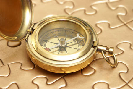 A brass compass rest on top of a golden jigsaw puzzle for different concepts.の写真素材