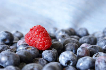 A fresh raspberry rests on a bunch of blueberries.の写真素材