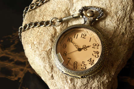 A macro shot of an antique pocket watch on a textured rock.の写真素材