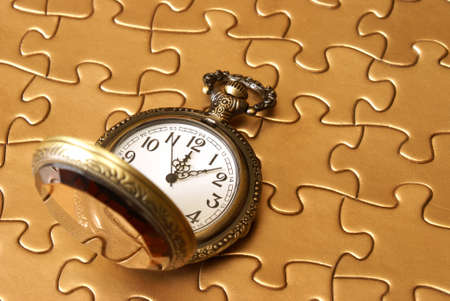 A pocket watch rests on a golden puzzle.の写真素材