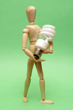 A wooden guy holds onto a modern cfl lightbulb for many ecological concepts.の写真素材
