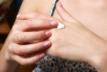 A young woman applies a small amount of moisturizer to her hands.