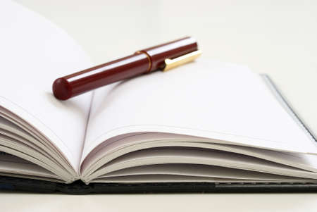 A closeup view of an elegant pen on top of an open journal with blank white pages.の写真素材
