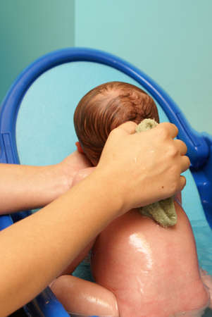 A newborn baby boy is getting his daily scrubbing at home in his infant tub with the tender care of...