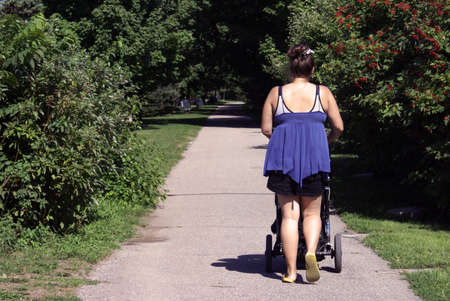 A loving Mother walks her newborn baby through the park on a bright sunshining day.