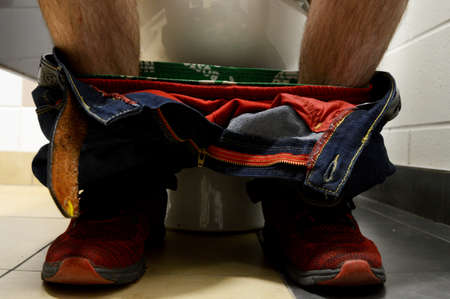 An adult male sits down on the toilet to do his morning business.の写真素材