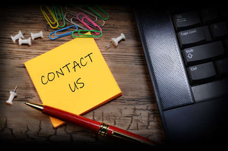 An overhead view of an assistants desktop with a handwritten note to Contact Us.の写真素材