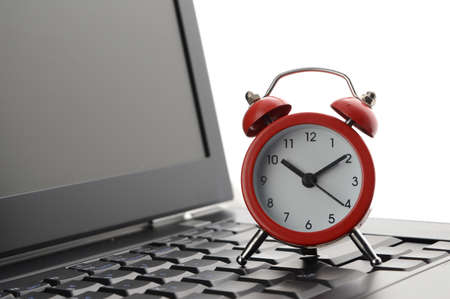 A closeup composition of a laptop and a red alarm clock to conceptualize on business deadlines.の写真素材
