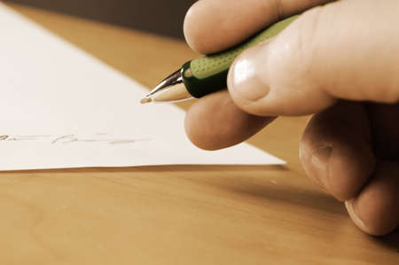 A vintage filter over an image of an important document is being signed by the appropriate person with a closeup of their hand and focus on the tip of the ball point pen.の写真素材