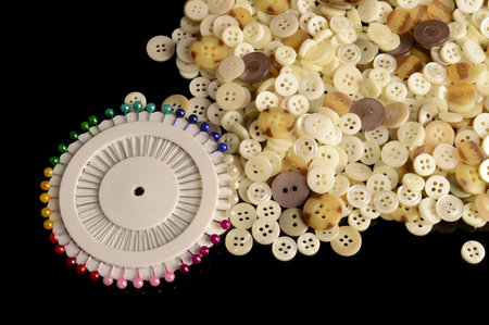 A closeup of sewing pins and buttons over a black reflective surface.