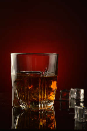 A closeup of a glass full of whiskey and ice over a dark red background with a shallow depth of field on the glass.の写真素材