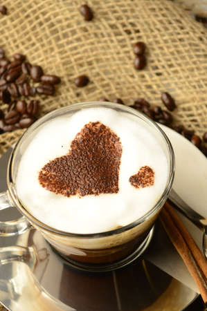A specialty cup of brewed coffee with a heart shape design while resting among roasted beans.の写真素材