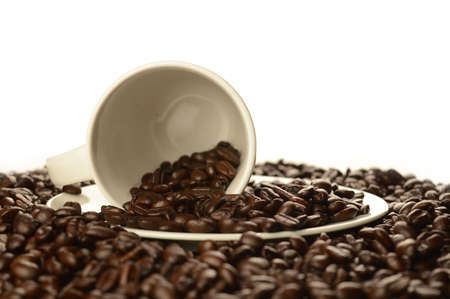 An abundant pile of coffee beans surrounds a white cup and saucer over a clean white background.の写真素材