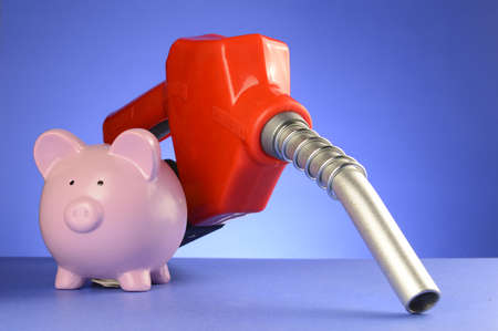 A concept of saving money at the gas pumps using a piggy bank and red fuel pump over a blue...