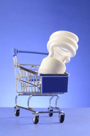 A CFL bulb is inside a miniature shopping cart over a blue background.の写真素材