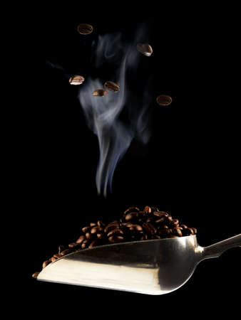 A scoop of freshly roasted coffee beans over a dark black background.の写真素材