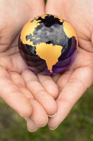 The Earth Globe is safely held inside the palm of a womans hands overtop of a grass area.の写真素材