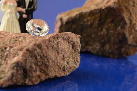 A bride and groom cake topper rest in the background of a focused brilliant cut diamond set for the occasion.の写真素材