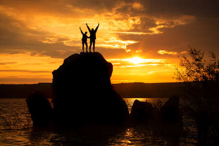 Happy pair silhouettes over sea and mountains, sunset.の写真素材