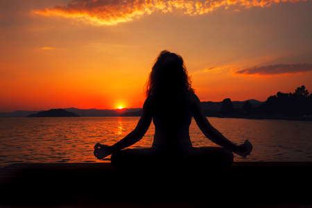 Woman silhouette meditation in tranquility over sunset on seaの写真素材