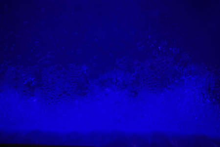 Foamy bubbles against a dark blue fluorescent backgroundの写真素材