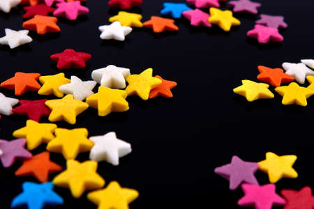 Colorful bright background, multi-colored stars. Sweet nice candy. Macro shoot photo on black glass...