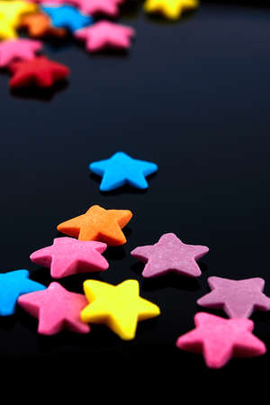 Colorful bright background, multi-colored stars. Sweet nice candy. Macro shoot photo on black glass backgroundの写真素材