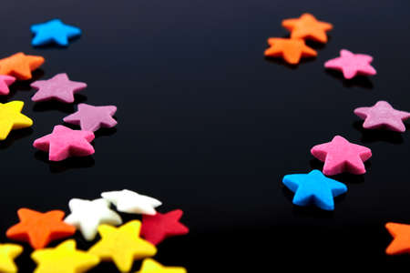 Colorful bright background, multi-colored stars. Sweet nice candy. Macro shoot photo on black glass backgroundの写真素材