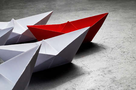 Business Concept, Paper Boat, the key opinion Leader, the concept of influence. One red paper boat as the Leader, leading in the direction of the white ships on a gray concrete background,copy spaceの写真素材
