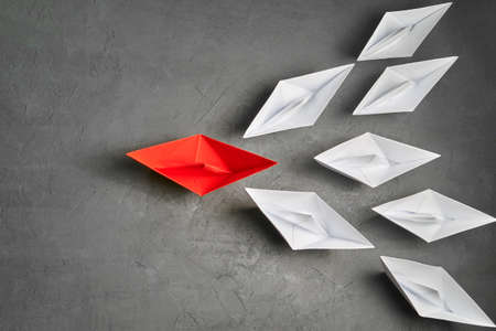 Business Concept, Paper Boat, the key opinion Leader, the concept of influence. One red paper boat as the Leader, leading in the direction of the white ships on a gray concrete background,flat lay,copy spaceの写真素材