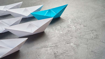 Business Concept, Paper Boat, the key opinion Leader, the concept of influence. One blue paper boat as the Leader, leading in the direction of the white ships on a gray concrete background,copy spaceの写真素材