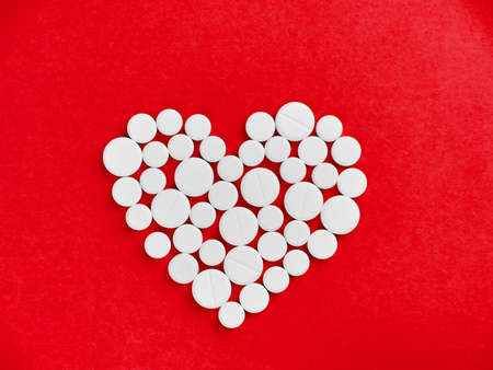 White pills in the shape of a heart on a red backgroundの写真素材