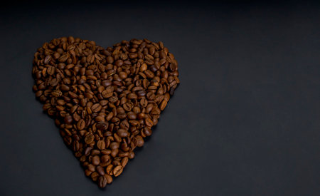 Roasted arabica coffee beans laid out in the shape of a heart, lie on a dark wooden background close upの写真素材