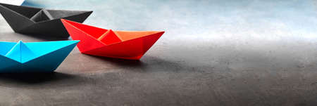 Red blue and black paper origami boats lie on concrete background. teamwork conceptの写真素材