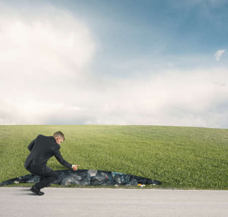 Businessman discovers garbage under a green fieldの写真素材