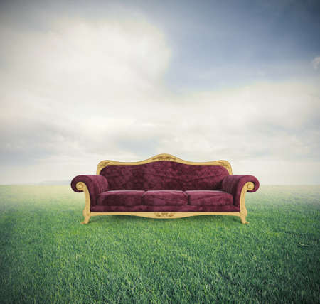 Concept of relax and comfort with a velvet red sofa in a green fieldの写真素材