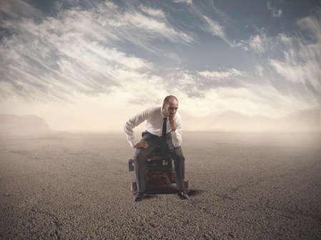 Concept of lost businessman confused sitting on suitcasesの写真素材