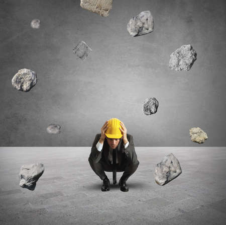 Frightened businessman under the storm of falling rocksの写真素材